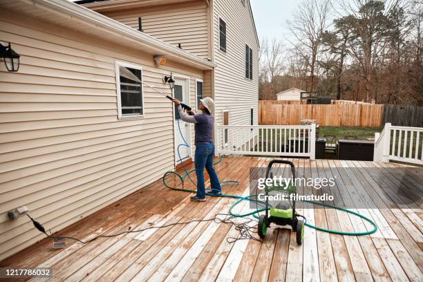 Latin woman using high water pressure cleaner to clean wall.